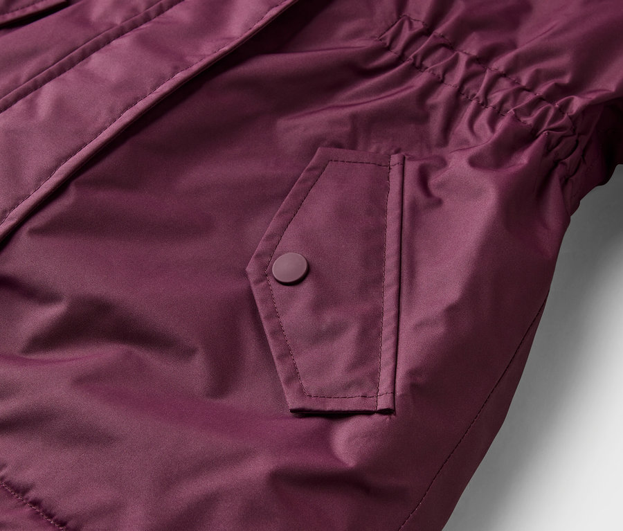 Gros plan d'une veste bordeaux, montrant une poche à rabat avec un bouton-pression et un détail élastiqué sur le côté.