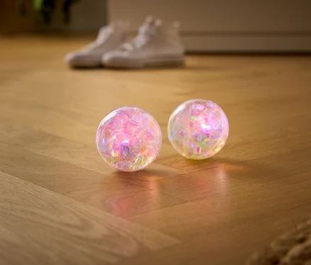 Deux boules transparentes et scintillantes reposent sur un parquet en bois, avec des baskets blanches floues en arrière-plan.