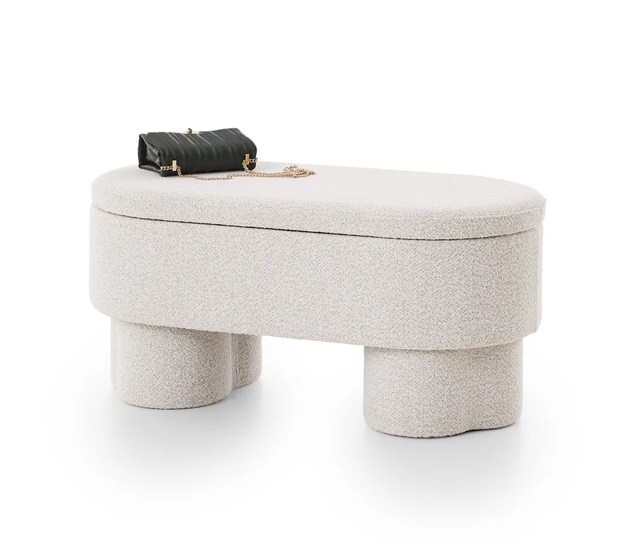 Ottoman allongé beige clair avec surface texturée et rangement, sur lequel repose un petit sac matelassé vert foncé avec une chaîne dorée.