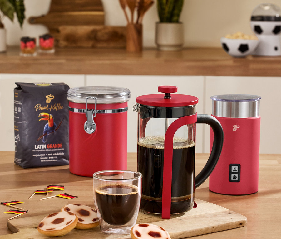 Sur une table, une boîte à arômes rouge, un mousseur à lait électrique rouge, une cafetière à piston rouge, 2 verres à double paroi pour café crème et un paquet de café.