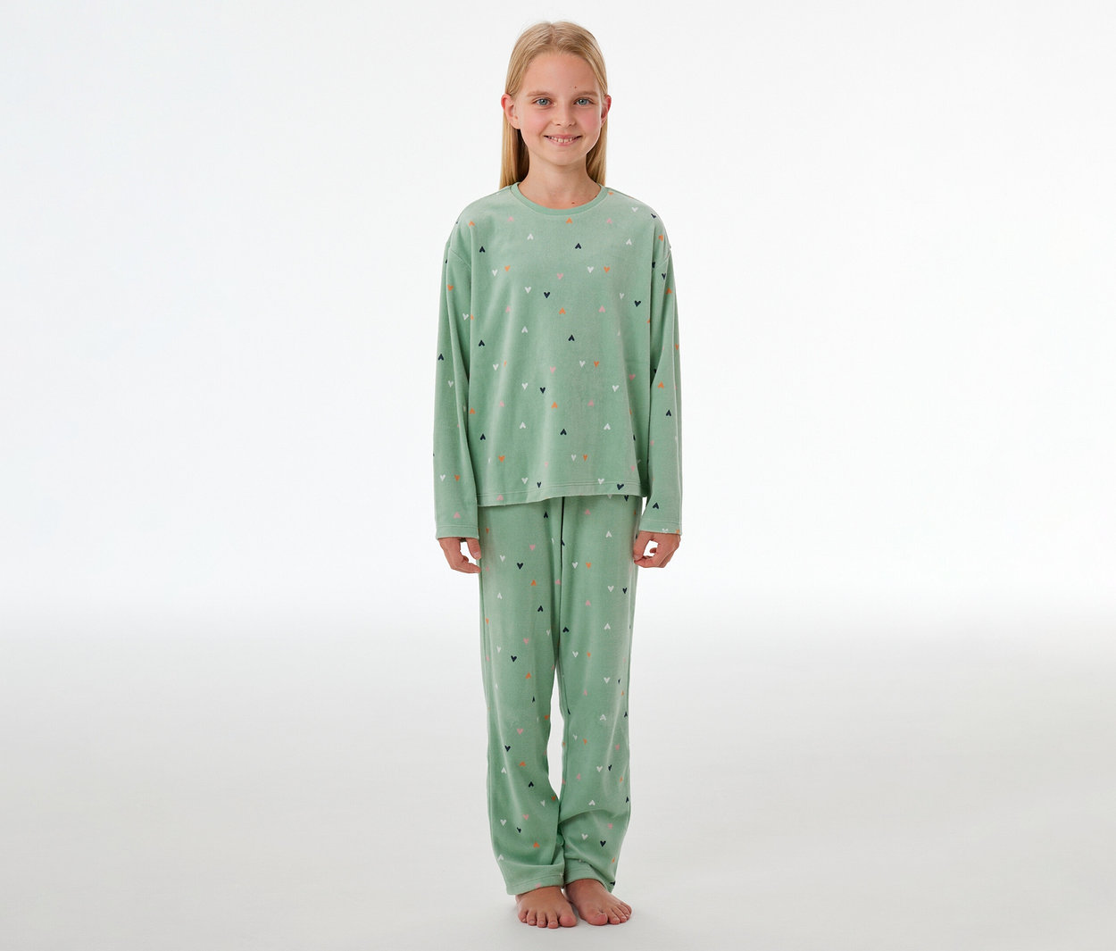 Fille souriante pieds nus en pyjama en velours vert clair à motifs de cœurs colorés.