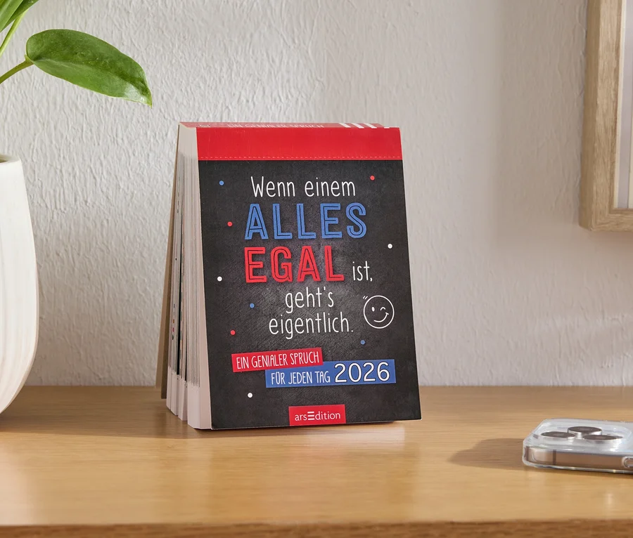 Calendrier de table avec l'inscription "Quand TOUT est ÉGAL à quelqu'un, ça se passe en fait en 2026", à côté d'un pot de fleurs et d'un téléphone portable sur la table.