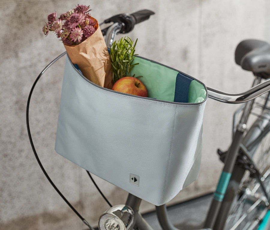 Une sacoche pour guidon de vélo est fixée au guidon d'un vélo. Dans la sacoche, il y a des fleurs, des herbes et une pomme.
