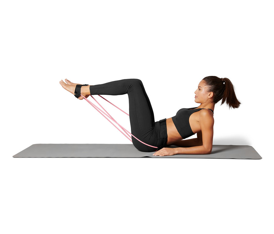 Une femme est allongée sur un tapis et fait de l'exercice avec une ceinture avec des élastiques de fitness attachés à ses pieds.