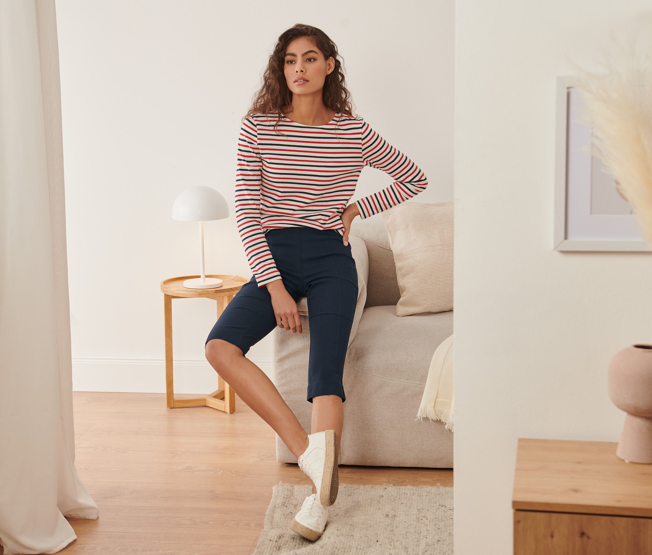Femme assise sur un canapé portant un corsaire stretch et un haut rayé.