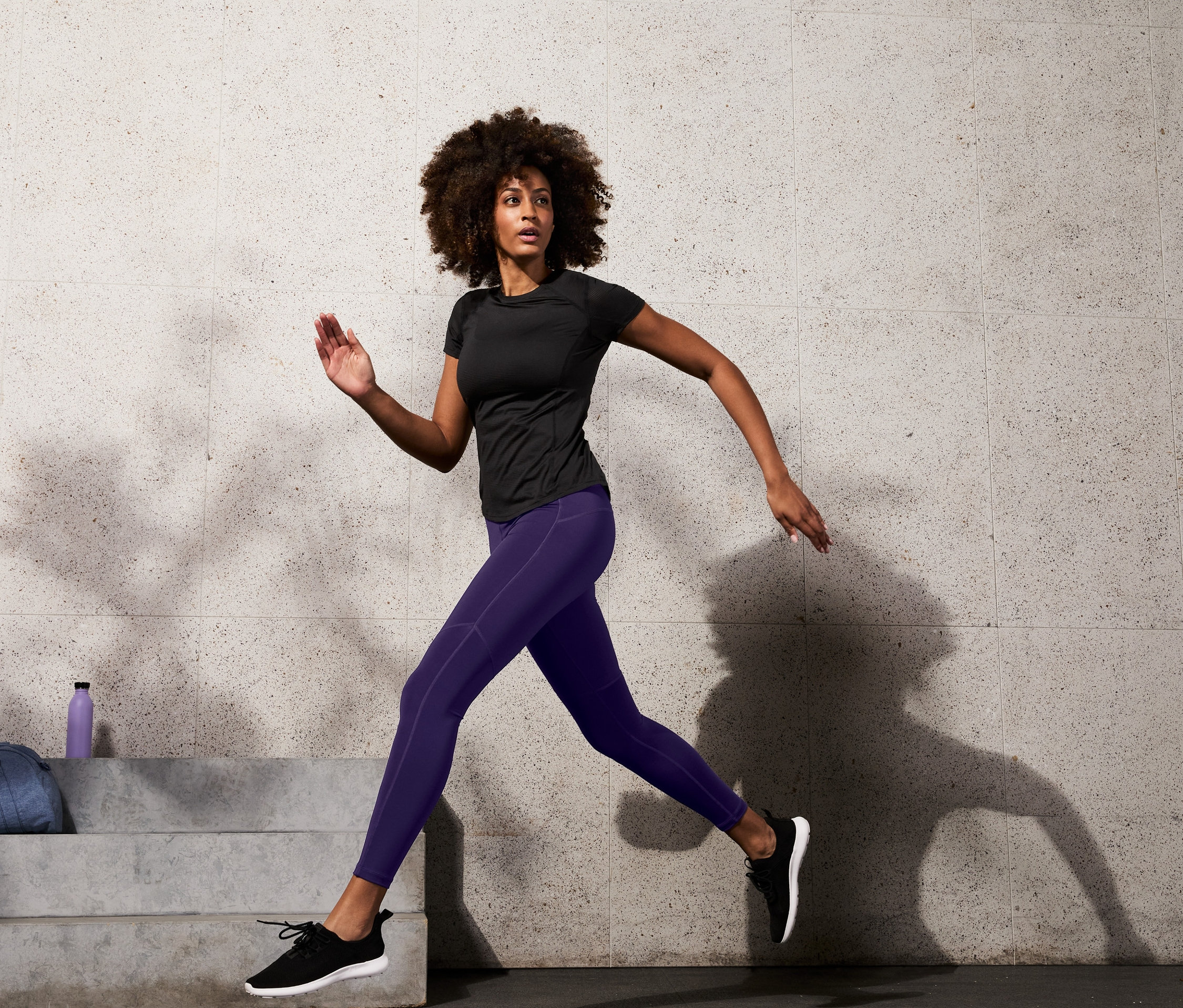 Femme courant en legging de sport modelant et haut de sport noir.