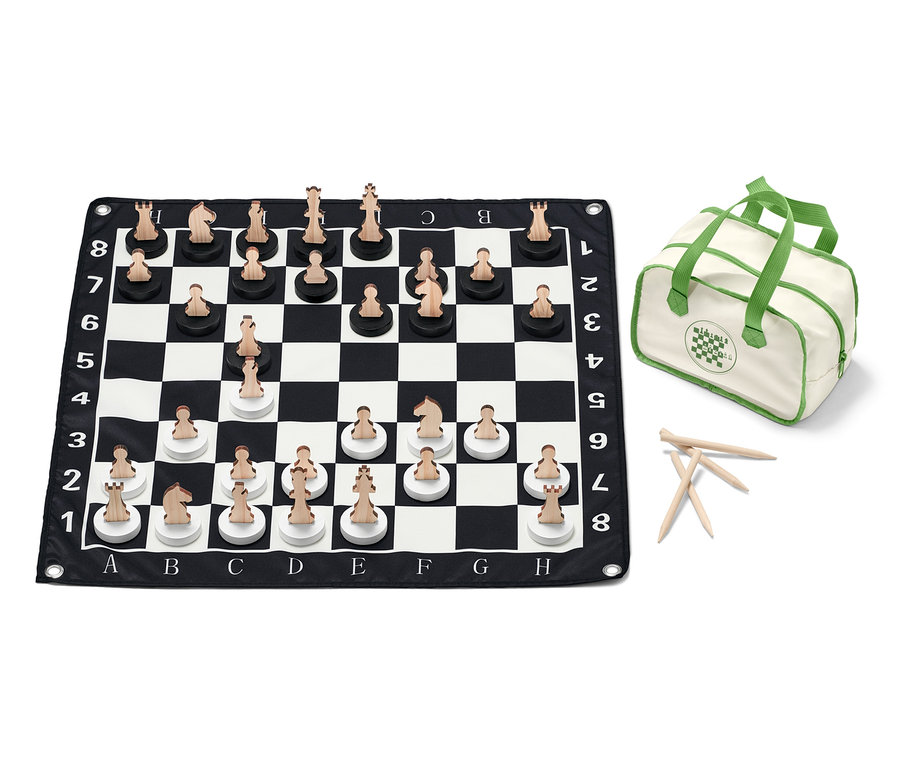 Un jeu d'échecs XL est disposé sur un échiquier noir et blanc avec des pièces en bois, et il y a un sac à côté.