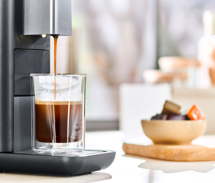Le café coule d'une machine à café Qbo ESSENTIAL Dark Stone dans un verre.