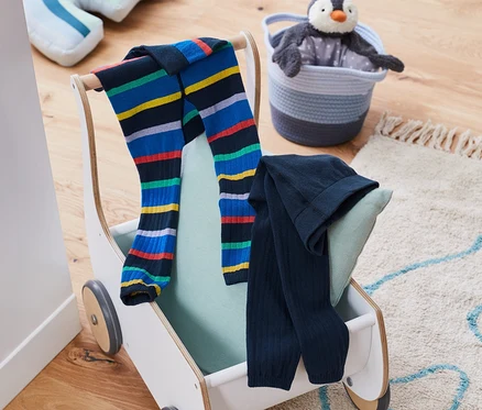 Deux leggings en maille sont posés sur un chariot à jouets à côté d'un manchot en peluche dans un panier.