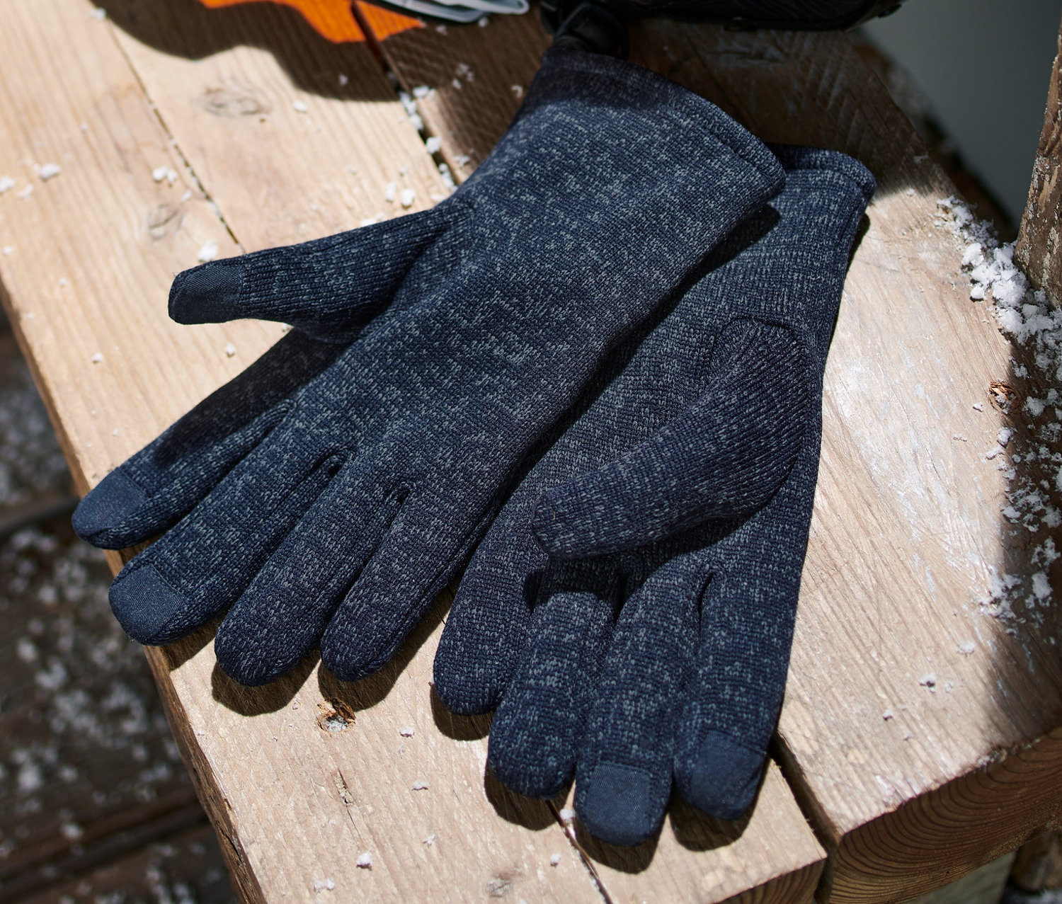 Une paire de gants en polaire tricotée bleu foncé est posée sur un banc en bois.