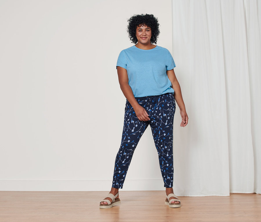 Une femme debout porte un t-shirt bleu clair en lin mélangé, un pantalon en jersey bleu foncé à imprimé intégral et des sandales à plateforme en cuir.