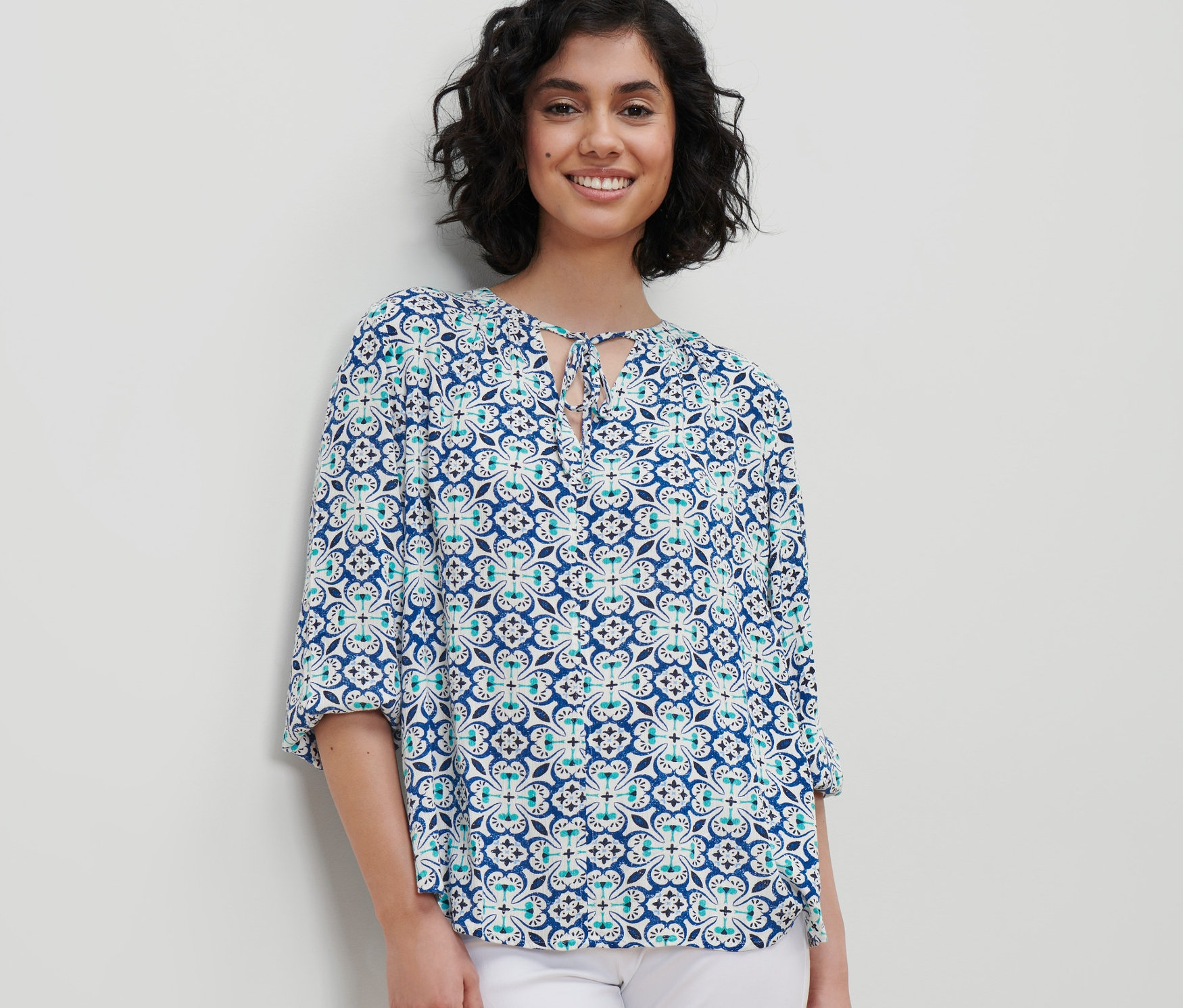 Une femme porte un chemisier-tunique avec un imprimé intégral et un pantalon blanc.