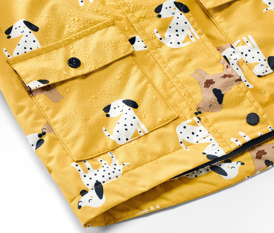 Gros plan sur une veste de pluie thermique jaune pour enfant avec un imprimé dalmatien et des gouttes d'eau.