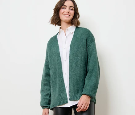 Une femme porte un cardigan ouvert en grosse maille.