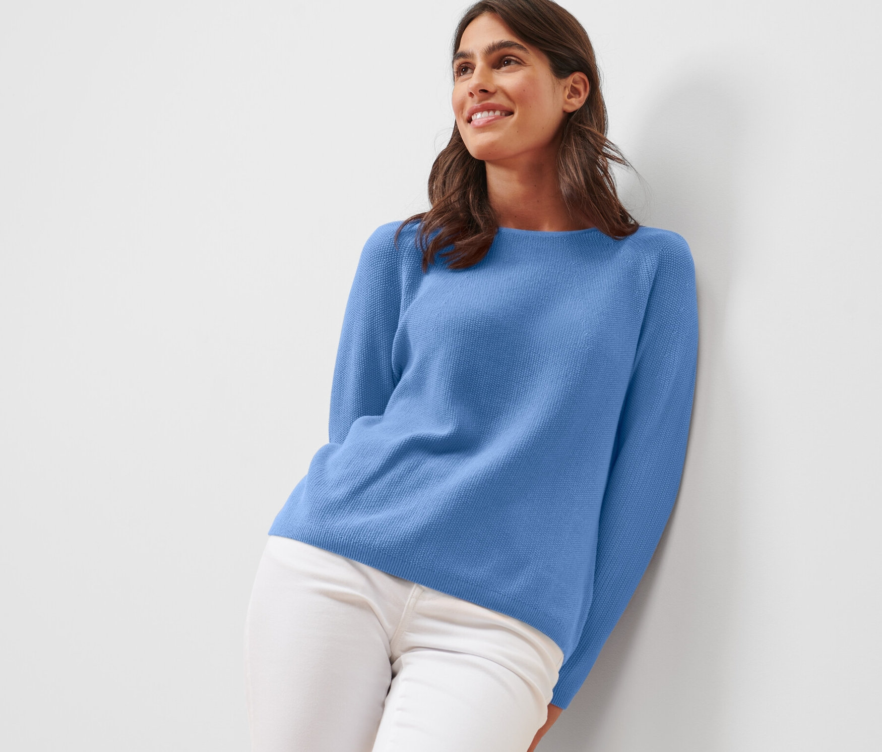 Femme appuyée contre un mur portant un pull en maille bleu.