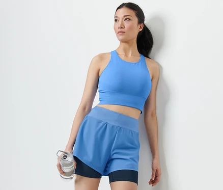 Femme en soutien-gorge de sport bleu et short de sport 2 en 1 tenant une bouteille d'eau.