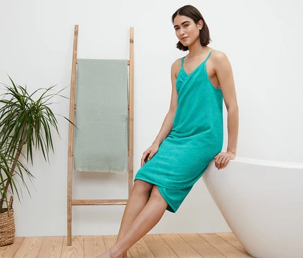 Femme assise sur le bord de la baignoire et portant une robe-serviette turquoise.