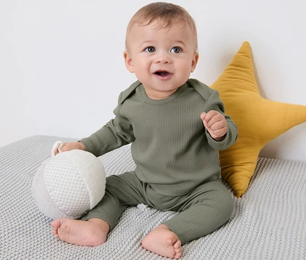 Un bébé est assis sur une couverture grise à côté d'une étoile jaune. Il porte un des 3 t-shirts côtelés pour bébé.