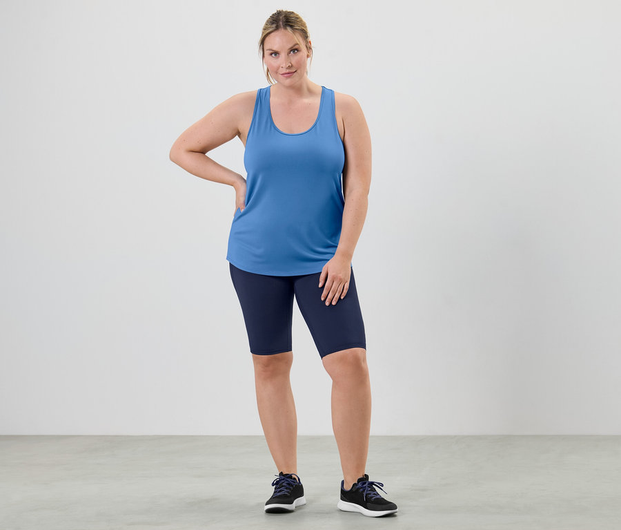 Une femme pose dans un top technique bleu ciel d'un ensemble deux pièces et un short de cycliste.