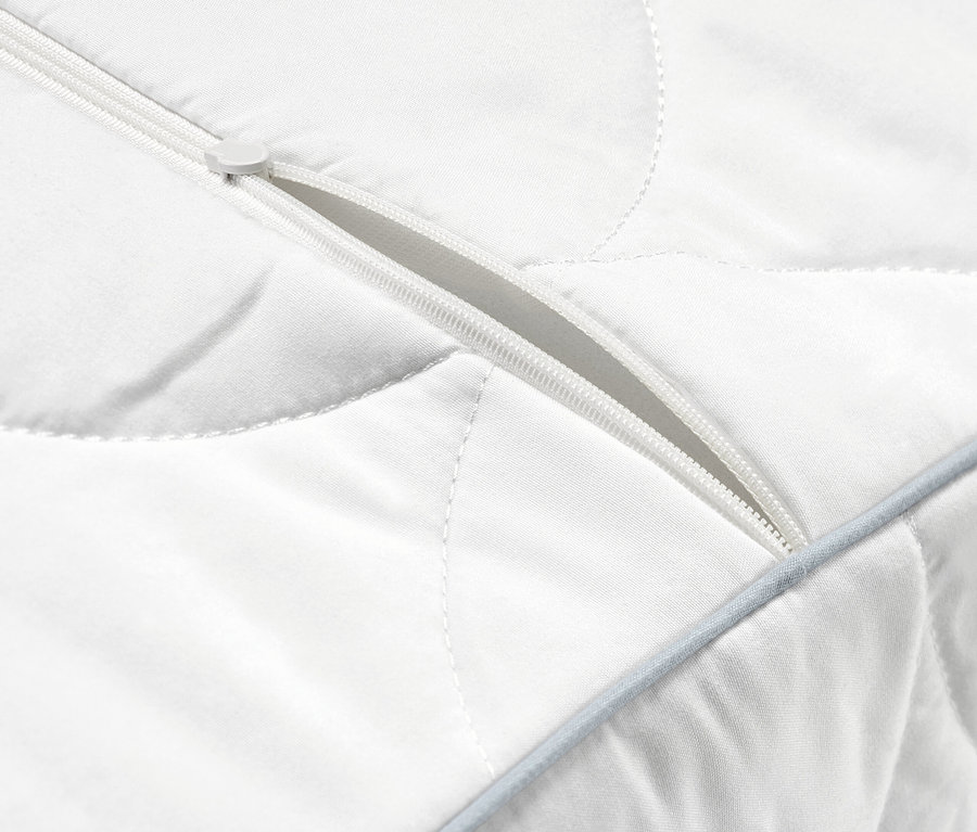 Gros plan sur un oreiller cervical blanc matelassé avec une fermeture éclair partiellement ouverte.