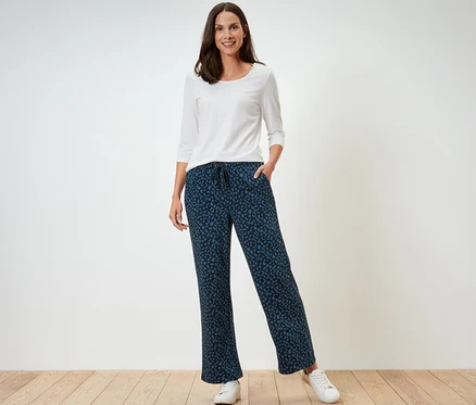 Une femme debout porte un t-shirt blanc à manches longues et un pantalon doux imprimé.