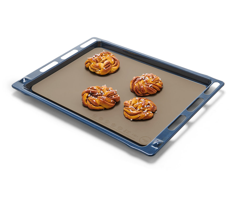 Quatre brioches à la cannelle sur un tapis de cuisson double face sur une plaque de cuisson bleue.