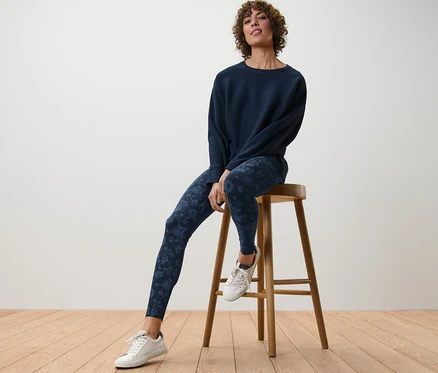Femme assise sur un tabouret en bois portant un legging à imprimé.