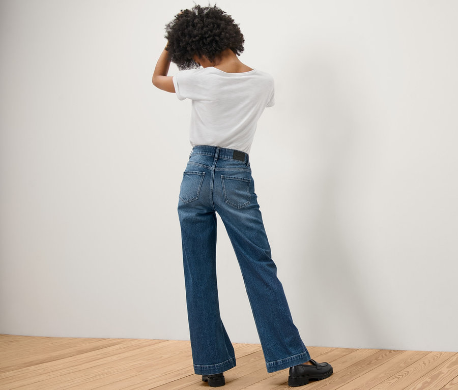 Vue arrière d'une femme aux cheveux afro debout, les mains dans les cheveux. Elle porte un Jeans Wide Leg – Fit « Viki » et un t-shirt blanc.