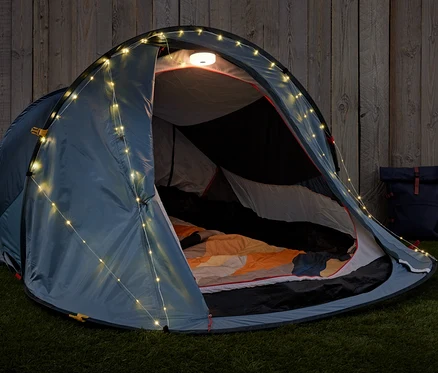 Tente ouverte avec guirlande lumineuse de camping 2 en 1 et sac à dos sur l'herbe.