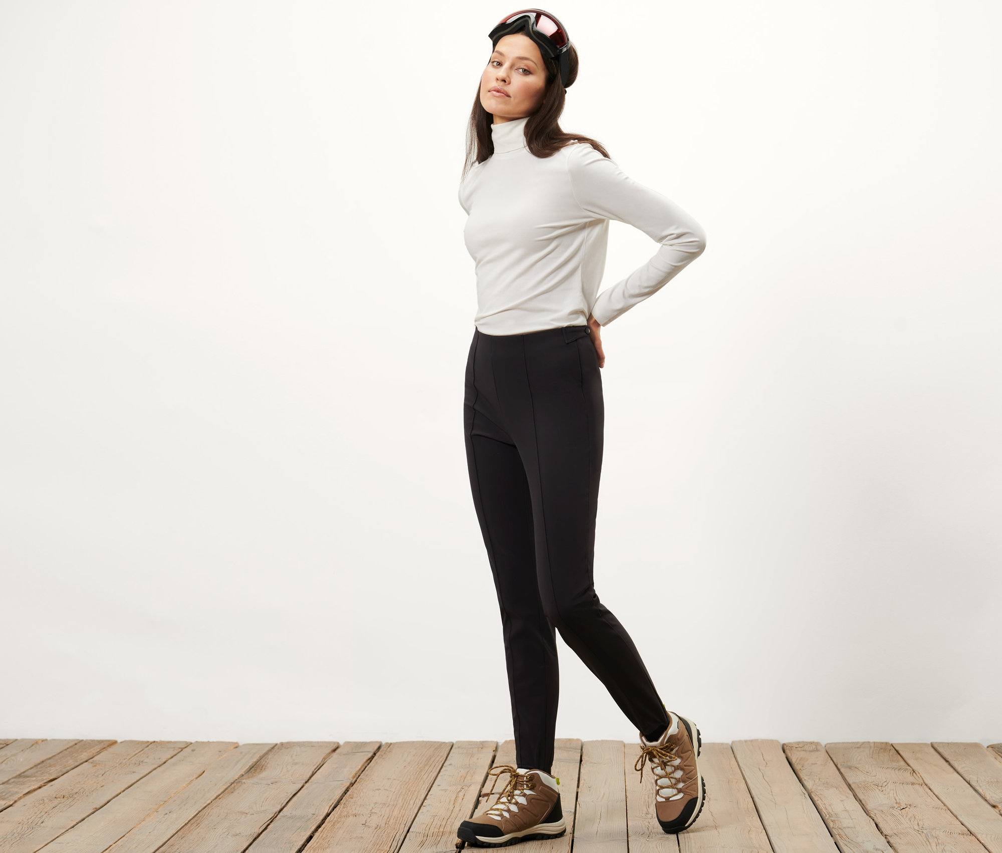 Femme posant en collant de ski softshell, col roulé blanc et lunettes de ski.