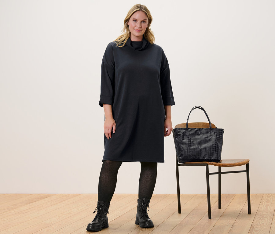 Une femme debout porte une robe en sweat en mélange de modal et un collant structuré en maille. À côté d'elle se trouve une chaise avec un sac à main dessus.