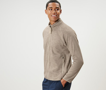 Un homme pose en cardigan en polaire beige et pantalon bleu marine.