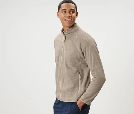 Un homme pose en cardigan en polaire beige et pantalon bleu marine.