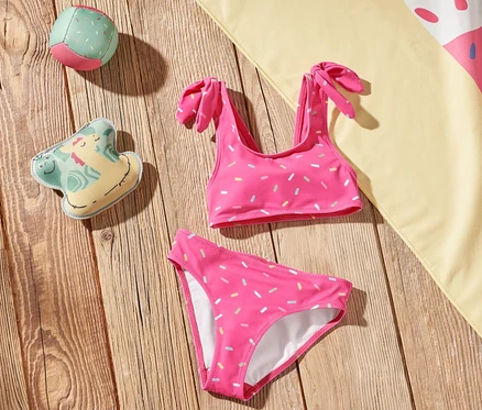 Sur un plancher en bois reposent un bikini pour enfants, une serviette de plage à motif de crème glacée et des jouets.