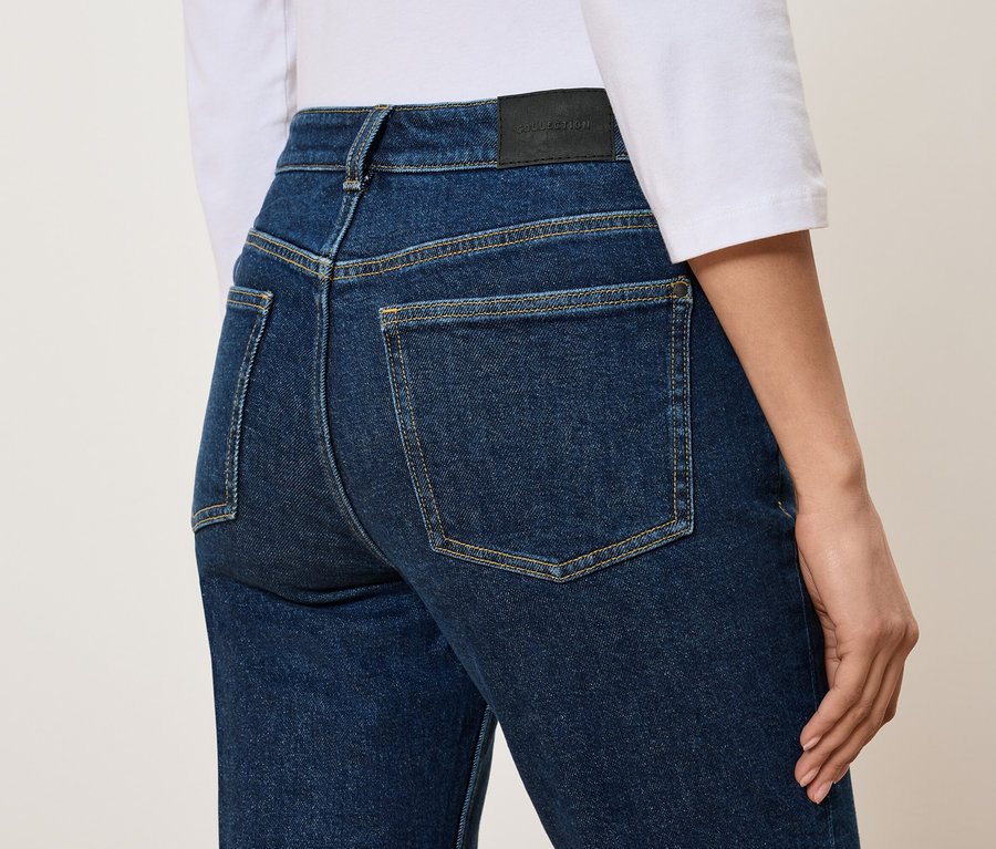 Vue arrière d'une femme portant un jean bleu taille haute et un t-shirt blanc.