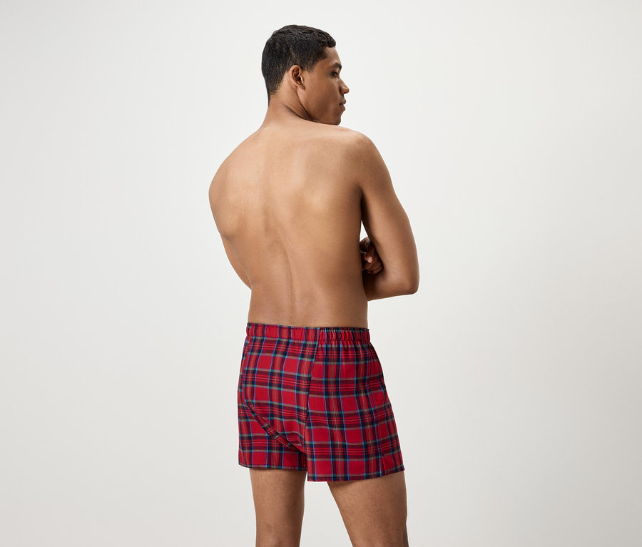 Un homme, dos à la caméra, porte un caleçon boxer à carreaux rouges.