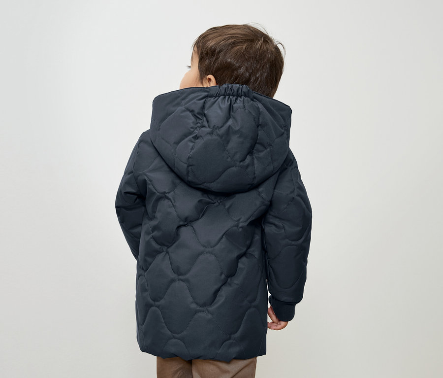Garçon portant une veste matelassée bleu foncé à capuche, dos à la caméra.