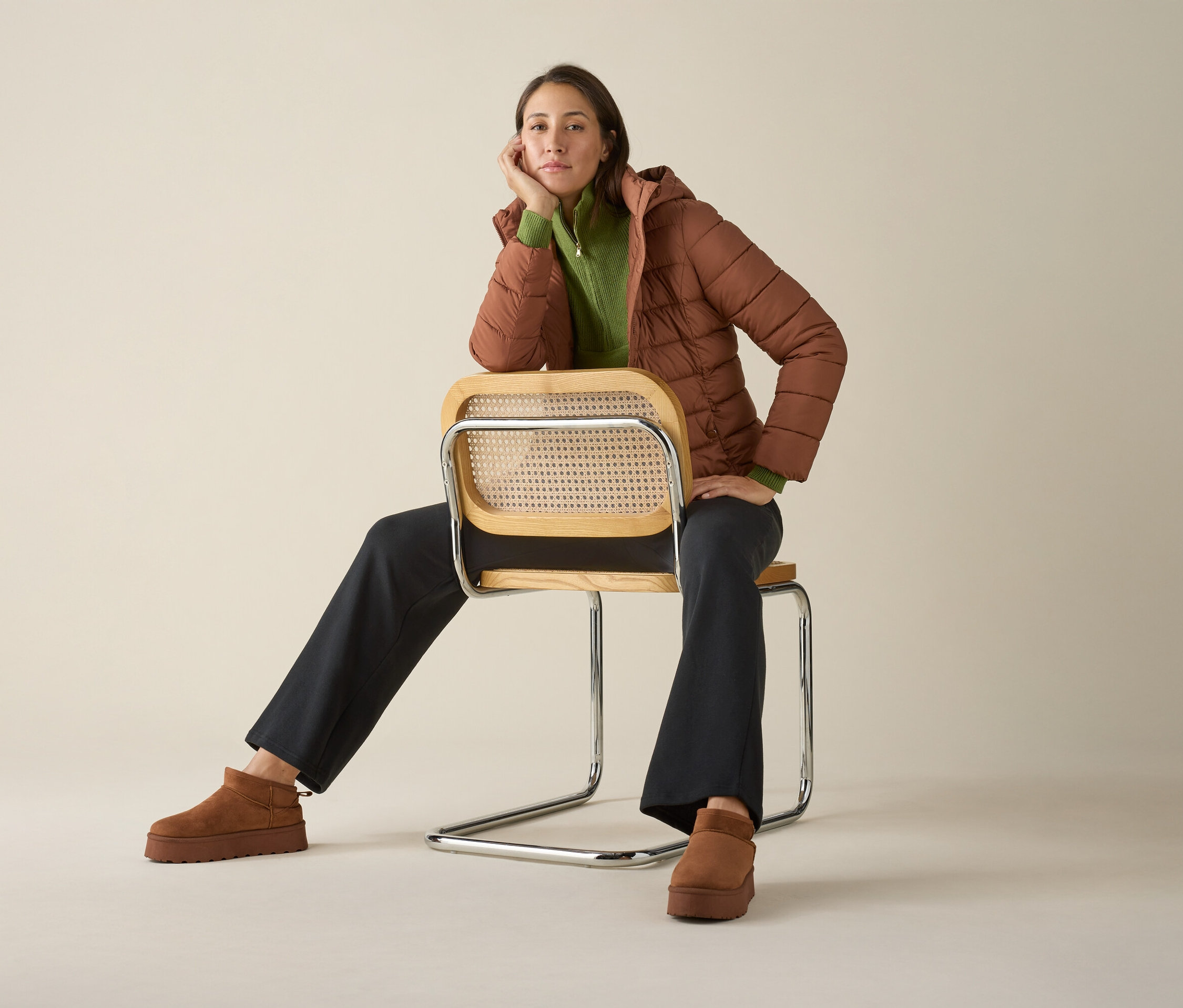Une femme est assise sur une chaise portant un pull camionneur en tricot, une veste et des chaussures.