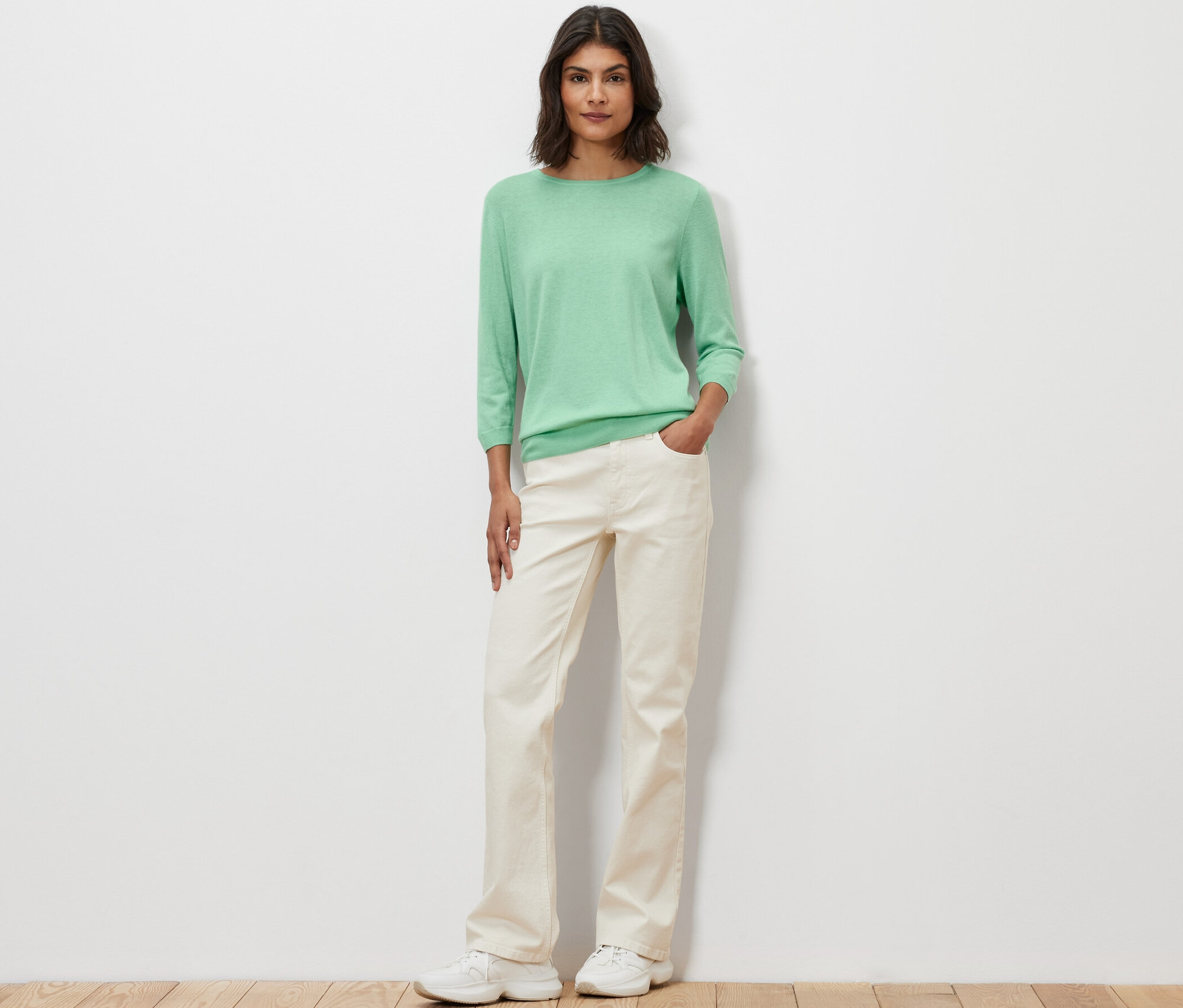 Une femme pose et porte un pull-over en maille fine vert clair avec de la soie.