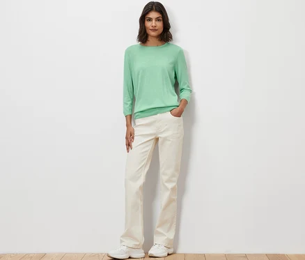 Une femme pose et porte un pull-over en maille fine vert clair avec de la soie.