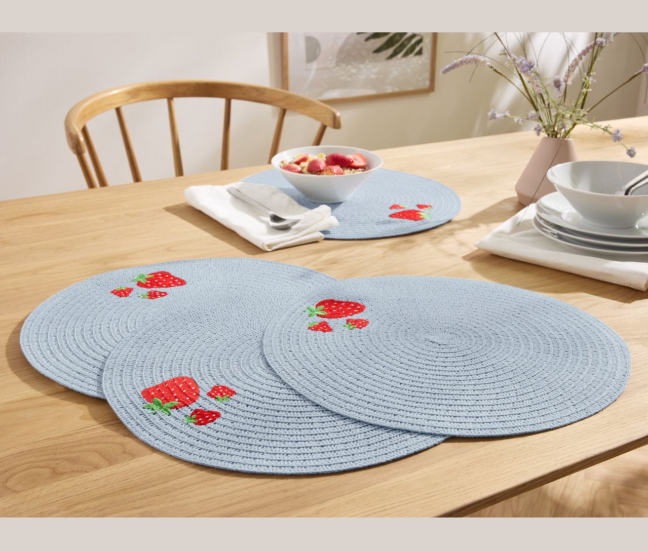 Quatre sets de table bleus avec des fraises sur une table en bois.