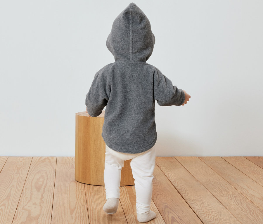 Un enfant, vu de dos, porte une veste en polaire grise pour bébé avec une capuche.