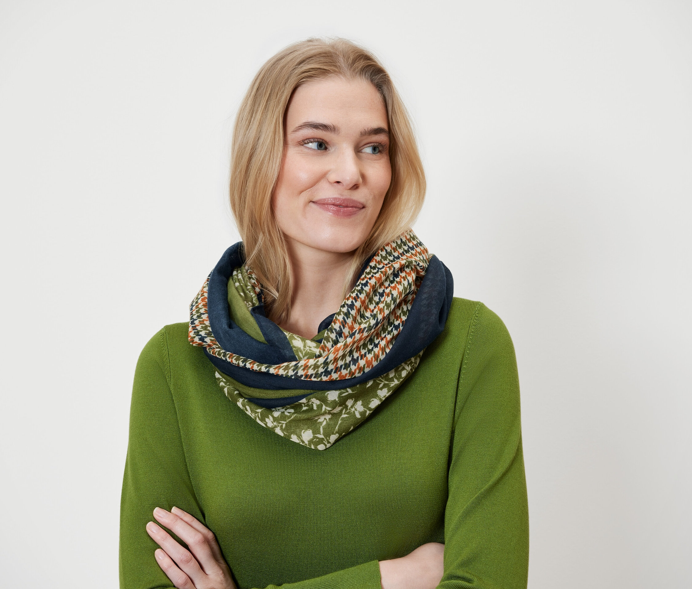 Une femme blonde porte un foulard multicolore et un pull vert.