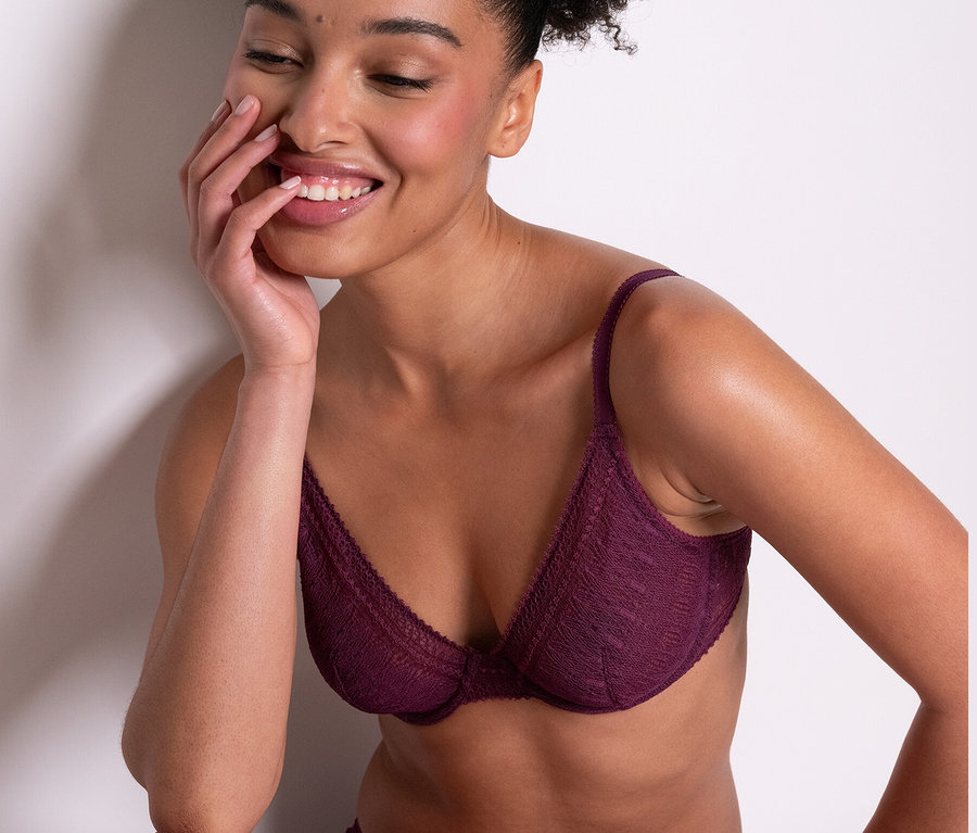 Une femme souriante est assise et porte un soutien-gorge à armatures «
Leila
» Passionata violet et des bas assortis.