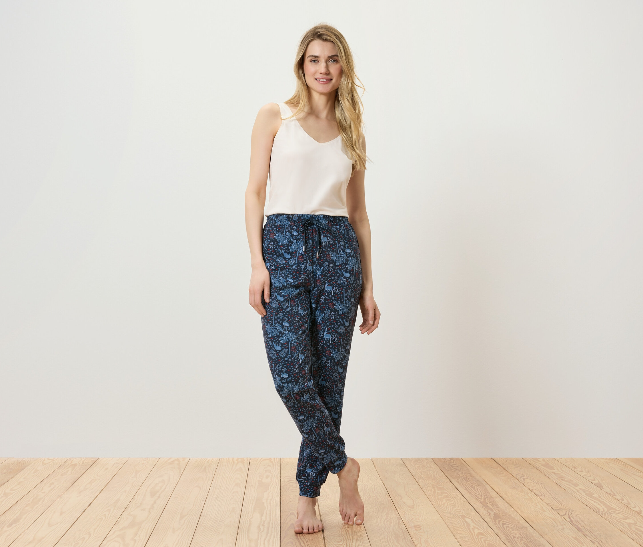 Une femme pose en débardeur et pantalon à motifs sur un plancher en bois.