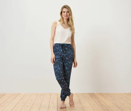 Une femme pose en débardeur et pantalon à motifs sur un plancher en bois.
