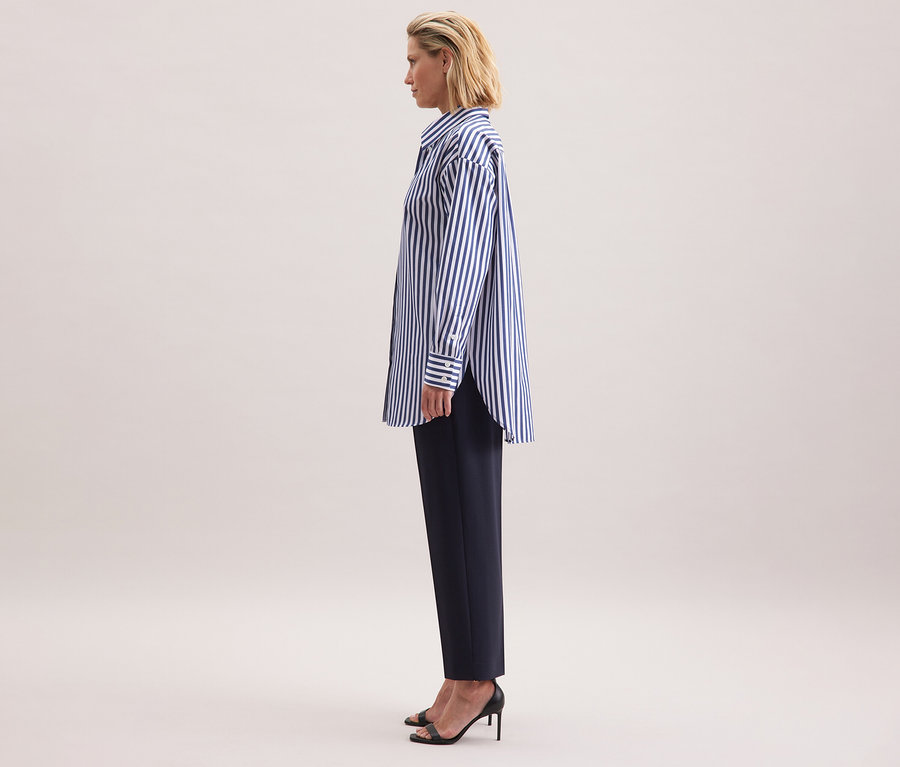 Femme portant une blouse-chemise grande taille Seidensticker à rayures, un pantalon foncé et des sandales noires.