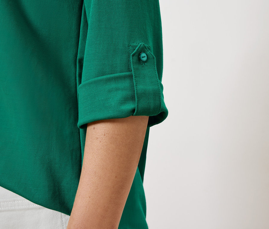 Gros plan sur une chemise verte à manches retroussées maintenues par un bouton.