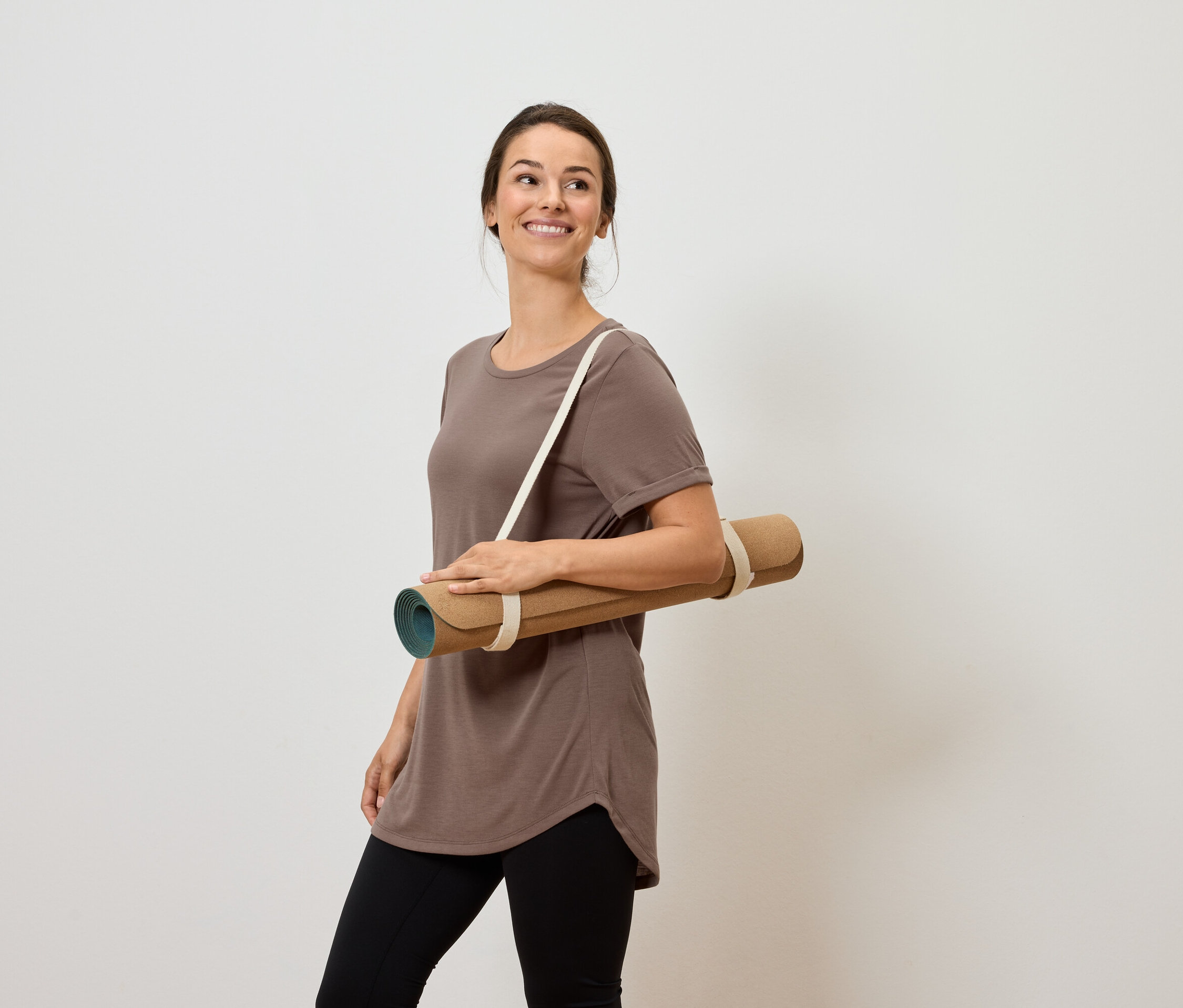 Femme souriante portant un tapis de yoga sur l'épaule.