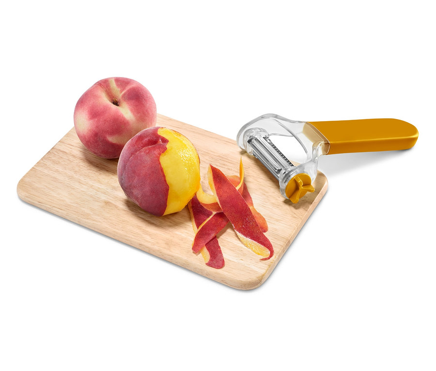 Deux pêches, dont une épluchée avec un éplucheur jaune sur une planche à découper en bois.